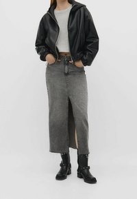 Veste zippée en simili cuir noir portée sur un t-shirt court gris, associée à une jupe midi en denim gris avec une fente avant et des bottines noires.