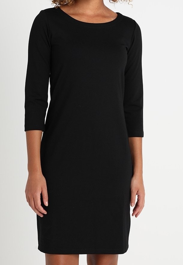 Femme vêtue d'une robe noire simple longueur genoux avec des manches trois-quarts et un col rond sur un fond blanc uni.