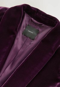Lila Samtjacke mit glatter Oberfläche und satinierter Innenseite. Verfügt über einen Reverskragen und ein schwarzes Etikett mit "NEXT"-Markenaufdruck.
