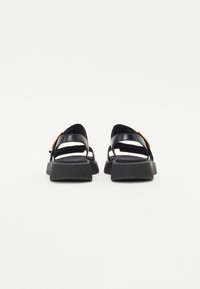 Black leather sandals with a wide strap design, textured black rubber sole, and a circular accent detail on the side.