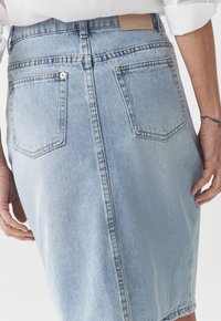 Lichte blauwe denim kokerrok met hoge taille, achterzakken en een leren label. Glad textuur met gestikte accenten.