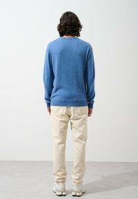 Blaues Sweatshirt mit strukturierter Oberfläche, Rundhalsausschnitt und langen Ärmeln, kombiniert mit cremeweißen Hosen und grauen Sneakern.