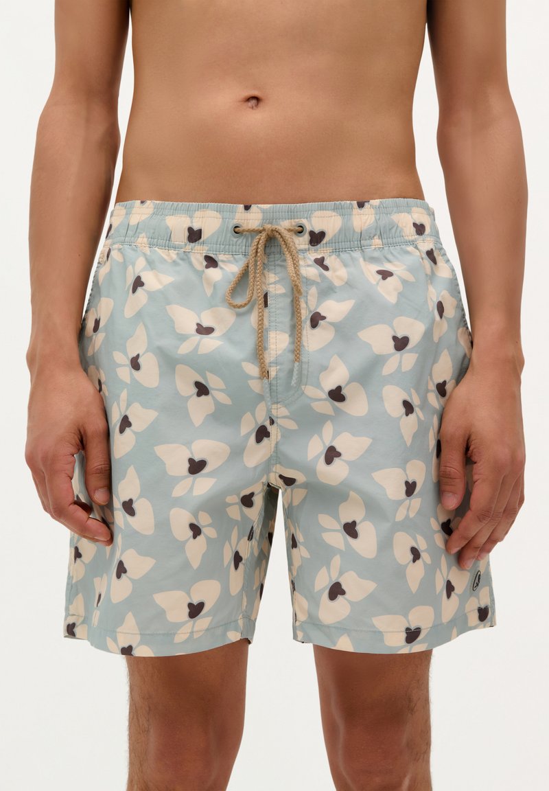 Shorts de bain bleu clair avec de grands motifs floraux crème et marron foncé. Dotés d'une taille élastique avec cordon de serrage et de poches latérales.