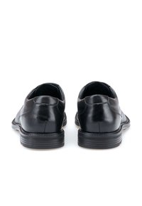 Chaussures en cuir noir avec une texture lisse, des coutures minimales et des talons arrondis. Semelles en caoutchouc à profil bas avec un détail de texture subtil.