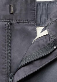 Braguette dézippée d'un pantalon gris foncé montrant une fermeture métallique à crochet et barre, une fermeture éclair et un tissu de doublure intérieure beige.