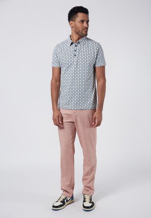 Camisa de manga corta con cuello, de base blanca y patrón geométrico azul, combinada con pantalones rosa claro y zapatillas negras.