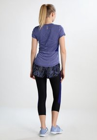 Lila tränings T-shirt med korta ärmar, ihop med svarta mönstrade shorts och svarta capribyxor. Skorna är ljusblå träningsskor.