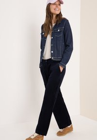 Dunkelblaue Denimjacke mit Fronttaschen und silbernen Knöpfen, kombiniert mit navyblauen Cordhosen und hellbraunen Sneakers.