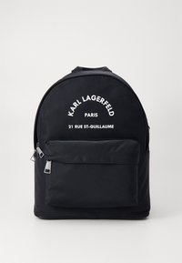 Sac à dos en nylon noir avec un haut courbé, poche à zip sur le devant et texte imprimé blanc. Comprend des tirettes de zip en argent et une texture lisse.
