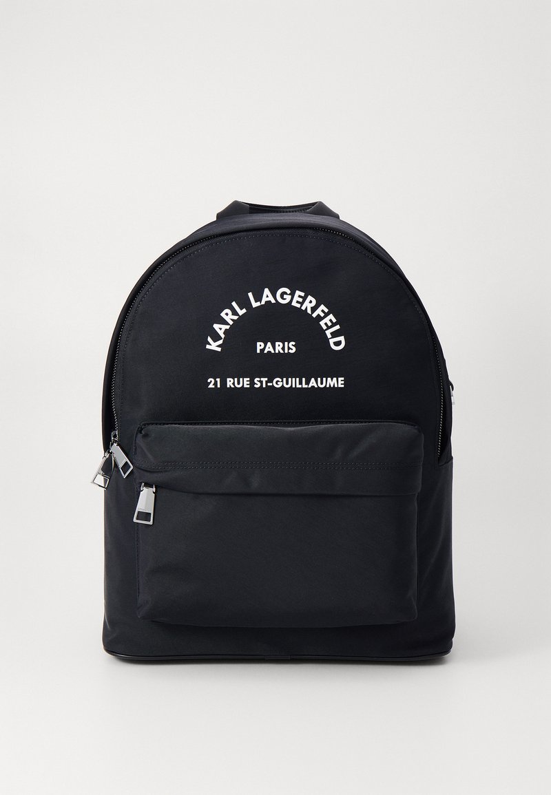 Sac à dos en nylon noir avec un haut courbé, poche à zip sur le devant et texte imprimé blanc. Comprend des tirettes de zip en argent et une texture lisse.