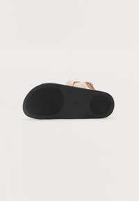 Sandale beige avec une semelle en caoutchouc noire, présentant une texture lisse et une boucle réglable sur la sangle.