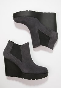 Stivali alla caviglia in suede grigio con pannelli laterali elasticizzati neri e suola nera spessa, caratterizzati da una punta rotonda e una texture liscia.