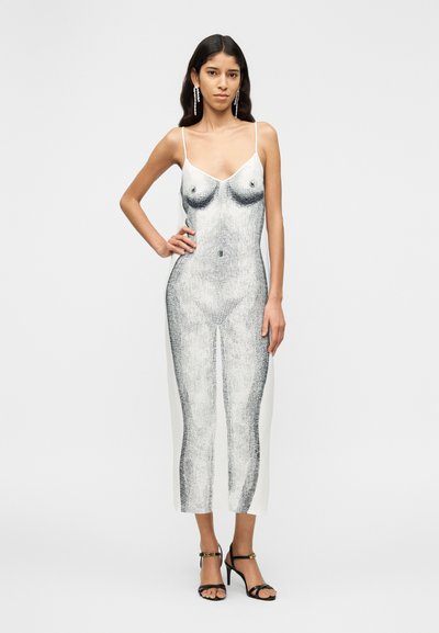 Λευκό φόρεμα με μαύρο σχέδιο στο σώμα, διαθέτει λεπτές τιράντες και εφαρμοστή σιλουέτα. Φορεμένο με μαύρα πέδιλα με λουράκια.