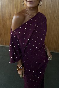 Bordó pliszírozott ruha vállvonás nélküli kialakítással, arany pöttyös mintával és széles ujjakal. Vastag karkötőkkel kiegészítve.