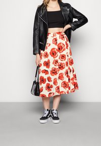 Musta lyhyt nahkatakki mustan topin päällä, yhdistetty kermaan vivahtavaan hameeseen, jossa on punaisia kukkakuvioita, sekä mustiin korkeavartisiin tennareihin.