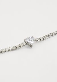 Bracciale in tonalità argento con un centro in gemma chiara a forma di cuore, circondato da piccole pietre rotonde chiare in una montatura a griffe.