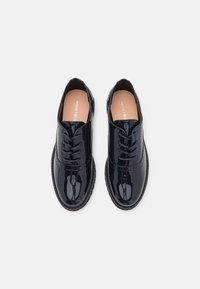 Scarpe stringate in vernice nera con punta arrotondata, superficie liscia e dettagli in cucitura lungo i lati. Suola in gomma leggera.