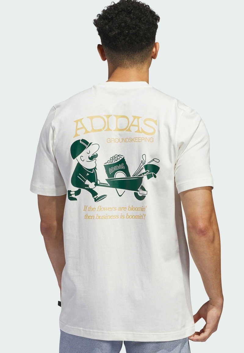 Bílý bavlněný tričko s grafickým potiskem karikaturního zahradníka, logem "ADIDAS", zelenými akcenty a žlutým textem na zádech.