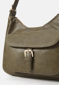 Sac à bandoulière en cuir vert olive avec un rabat frontal et des détails en boucle. Comprend une fermeture éclair dorée et des accents de couture. Texture lisse.