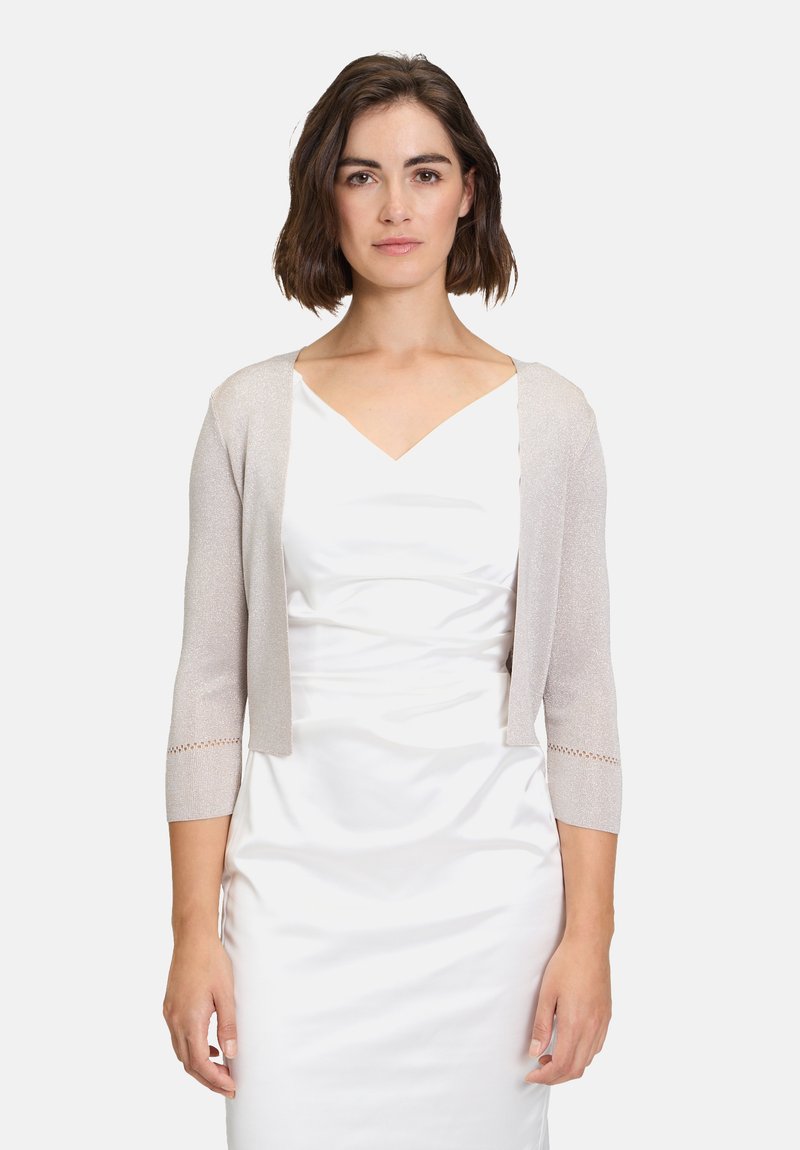 Rövid, világos bézs kardigán háromnegyedes ujjakkal és nyitott elülső résszel. Finom textúrájú részletekkel rendelkezik az ujjak végén.