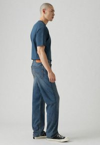 T-shirt blue in cotone a maniche corte abbinato a jeans blu chiari a gamba dritta. Sneakers in tela bianco e nero completano l'outfit.