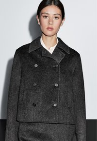 Giacca cropped in misto lana grigio con design doppiopetto, colletto a scollo a V, bottoni neri e trama sottile.