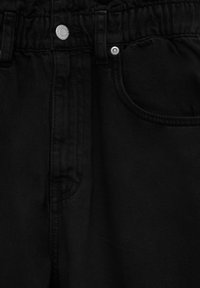 Les jeans en denim noir présentent une taille élastique, un design classique à cinq poches et des accents métalliques argentés, comprenant un bouton-pression et des rivets.