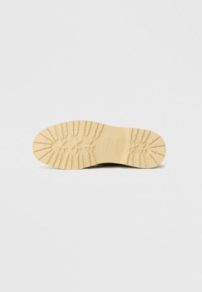 Beige värvivibram-kummipõhi, millel on ümmarguste nurgakestega mustrimuster ja logod, mis on loodud haardevõime ja vastupidavuse tagamiseks.