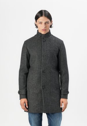 Abrigo de lana gris con un cuello alto, botones frontales y bolsillos laterales. Presenta una textura sutil y un ajuste entallado. Llevado sobre jeans azules.