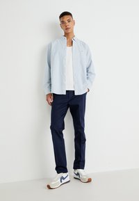 Chemise à rayures bleu clair, t-shirt blanc, pantalon navy et baskets blanches avec des accents bleus. Tenue décontractée avec des textures variées.
