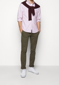 Ljusrosa och vita randiga skjorta, olivgröna byxor, vinröd tröja knuten runt axlarna, och vita sneakers. Avslappnad outfit.