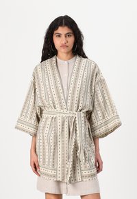 Vzorkovaný kimono v krémovej farbe s vertikálnymi pruhmi, ktorý obsahuje zelené a červené akcenty, opasok na viazanie a široké rukávy. Zloženie látky je z bavlnenej zmesi.