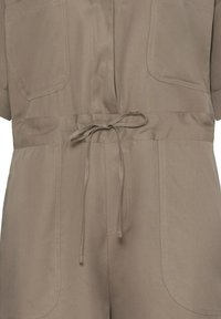 Combinaison taupe à manches courtes, poches plaquées à l'avant et ceinture en tissu nouée à la taille, réalisée en tissu sergé texturé.