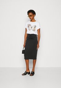 White t-shirt with butterfly and floral print, paired with a black, ruched pencil skirt. Black block-heeled mules and a small handbag complete the look.
