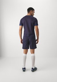 Jūrų laivyno sportinis džersis su trumpomis rankovėmis, mėlynos akcentai, derinamas su atitinkamomis šortais. Baltos iki kelių kojinės ir tamsūs futbolo batai su logo.