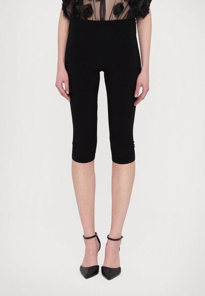 Leggings capri noirs avec un tissu lisse et extensible. Design taille haute avec une silhouette ajustée, se terminant juste en dessous du genou.