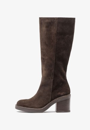 Bota de ante marrón hasta la rodilla con punta redondeada, tacón apilado y costura contrastante a lo largo de la suela. Textura suave y diseño elegante.