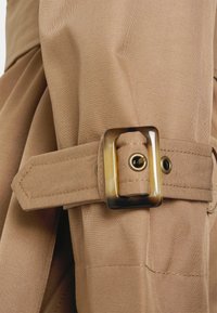 En tanfärgad tygbälte med en rektangulär spänne i sköldpaddsmönster. Materialet är slätt, med prydliga sömmar och en säker stängning.