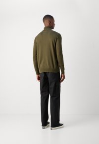 Maglione a maglia verde oliva con colletto alto, abbinato a pantaloni cargo neri e sneakers nere. Tessuto a trama fine e design aderente.