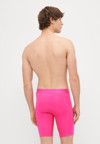 Ružové boxer šortky s priliehavým strihom a hladkou textúrou. Obsahujú logopás v zodpovedajúcej farbe. Strih do polovice stehien s plochými švami.
