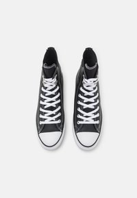 Zapatillas altas negras con punteras de goma blanca, cordones blancos y costuras en contraste. Textura suave, cuello acolchado y ojales de metal.