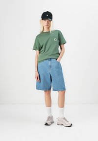Grønn bomull t-skjorte med brystlomme, blå denimshorts, svart caps, hvite sokker og lyserosa joggesko med mørke såler.