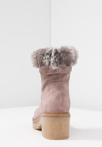 Pink suede ankle boot with a fur-lined cuff, featuring a chunky, textured heel and a smooth sole, highlighting a casual design.