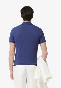 Polo de color azul marino con mangas cortas, cuello plano y tela texturizada. Combinado con pantalones blancos y una blazer crema colgada del brazo.