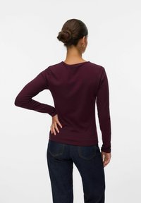 Långärmad, ribbad topp i djup vinröd, med rund halsringning och figurnära passform, ihop med mörka denimbyxor.