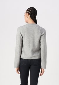 Suéter cinza de malha com gola redonda e mangas longas, apresentando um acabamento texturizado e bainha canelada, combinado com calças escuras.