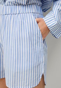 Blå og hvide stribede shorts lavet af let stof, med elastisk talje og sidelommer med en lille slidsdetalje ved kanten.