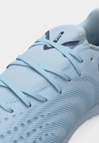 Svetlo modra športna obutev z usklajenimi vezalkami in temno modrim logotipom na jezičku, z teksturiranimi detajli na strani.