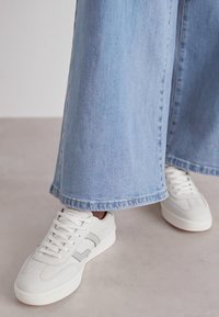 Valged sneakers hallide aktsentidega, koos laia säärega helesiniste teksadega. Teksadel on purunenud serv ja need on lõdva istuvusega.