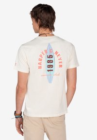 Camiseta de algodón color crema con un gráfico de una tabla de surf azul y texto rojo que dice "HARPER & NEYER 1985 club de verano" en la parte posterior.